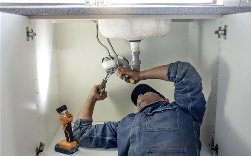 Plumber repairing pipes beneath a bathroom sink in Chandler