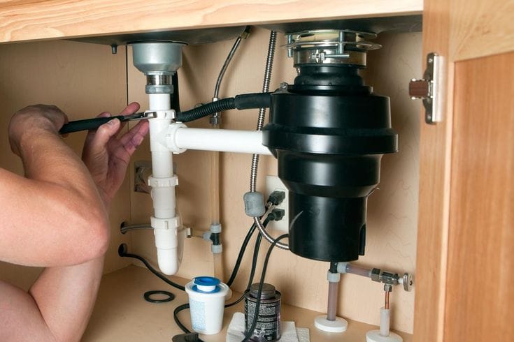 Plumber installing a garbage disposal beneath a kitchen sink in Chandler