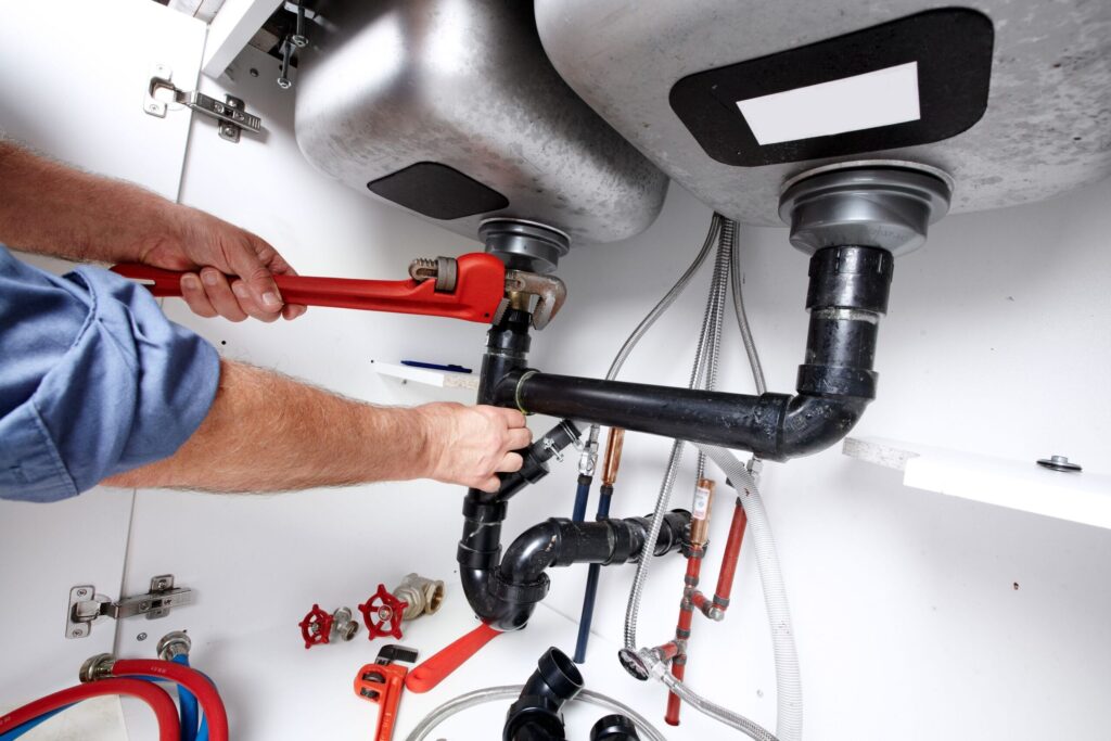 Plumber repairing drain pipes beneath a kitchen sink in Chandler